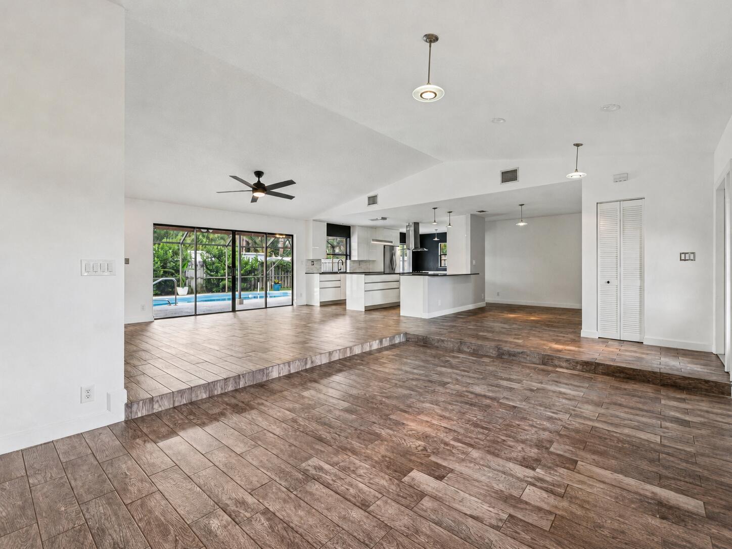 A sunken living area with wood-look tile floors leads to a kitchen and pool view — 17679 Woodview Terrace, Boca Raton FL 33487, BOCA RATON, FL