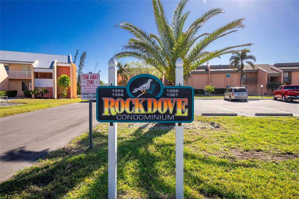 A sign for Rock Dove Condominium stands in front of apartment buildings and a parking lot — 1358 ROCK DOVE COURT UNIT 7, PUNTA GORDA, FL