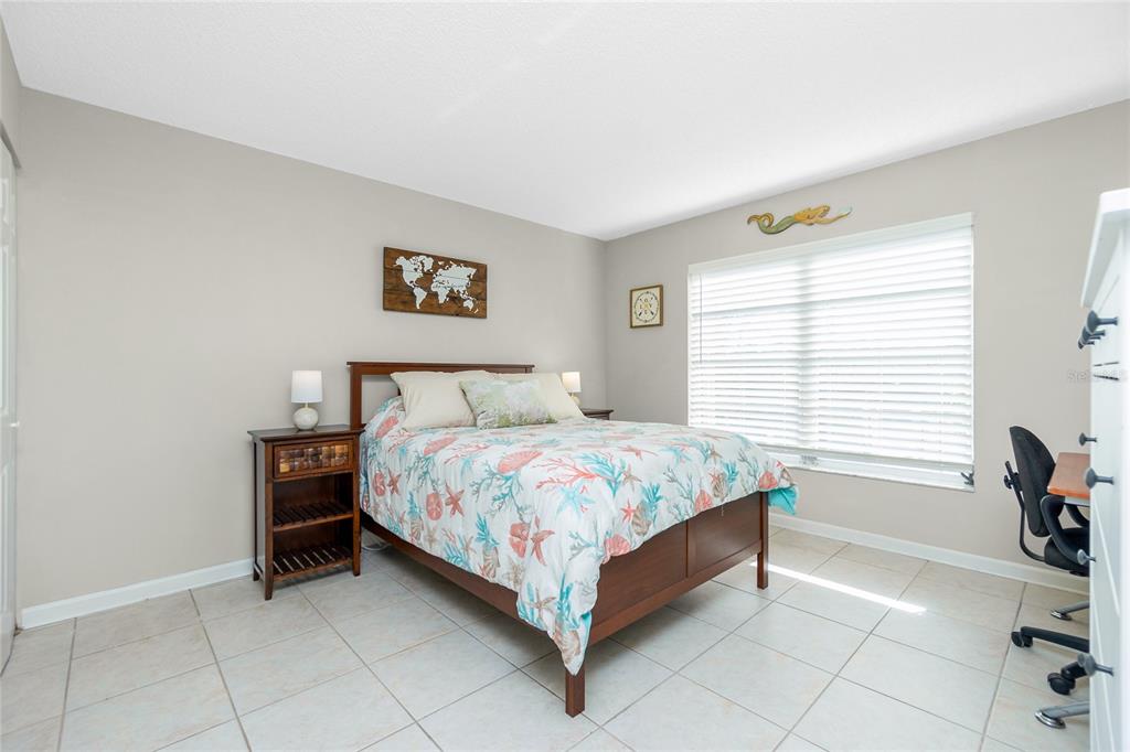 A bedroom features a bed with a seashell-patterned quilt, a wooden nightstand, and tile flooring — 1358 ROCK DOVE COURT UNIT 7, PUNTA GORDA, FL