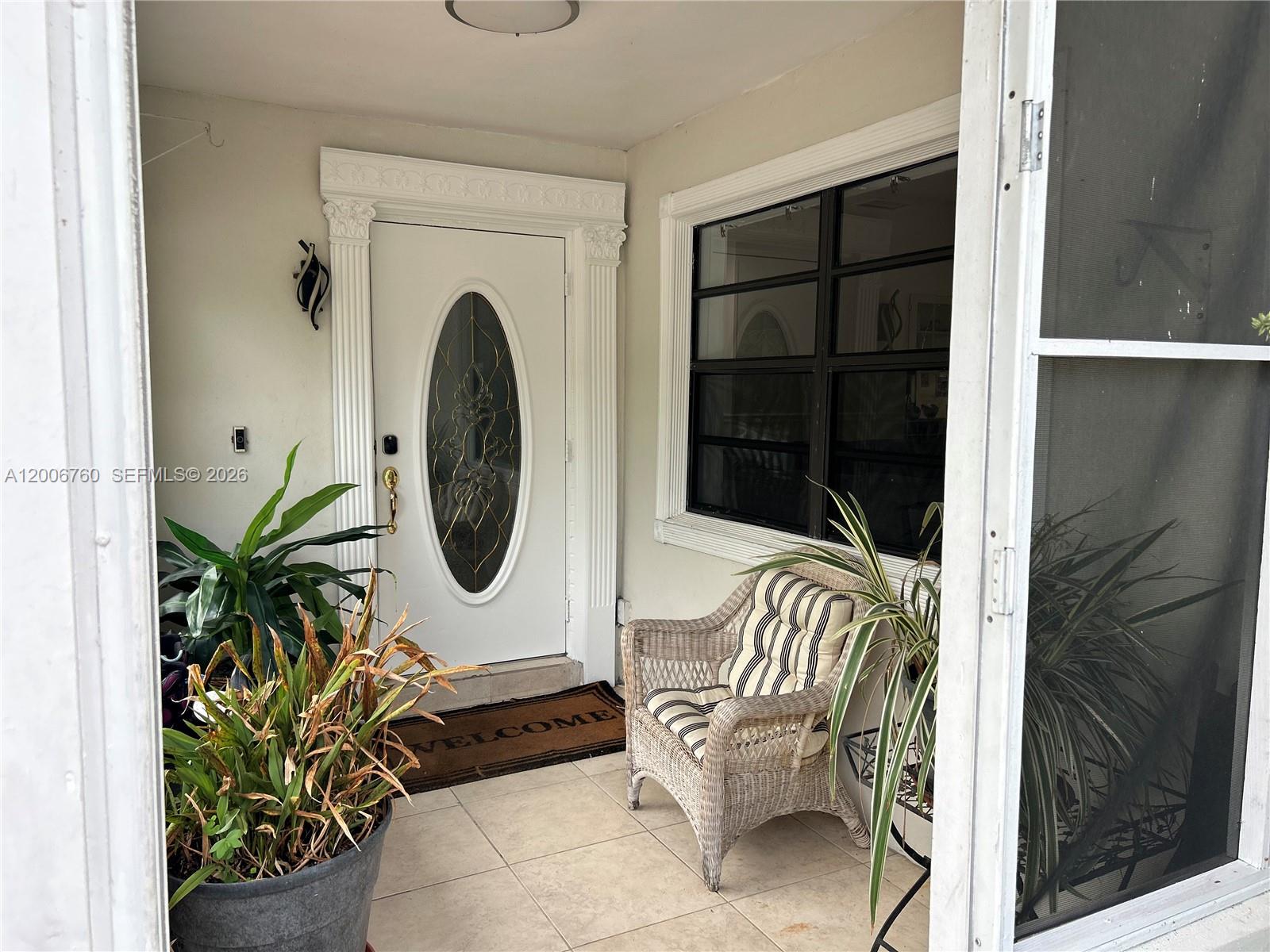 A covered porch features a white door with an oval glass insert and wicker seating — 11781 NW 14th St, Plantation FL 33323, PLANTATION, FL