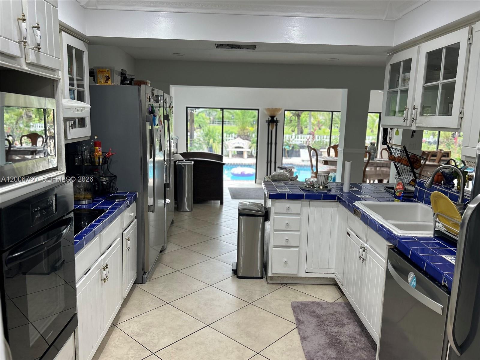 A kitchen features white cabinets, blue tiled countertops, stainless steel appliances, and a pool view — 11781 NW 14th St, Plantation FL 33323, PLANTATION, FL