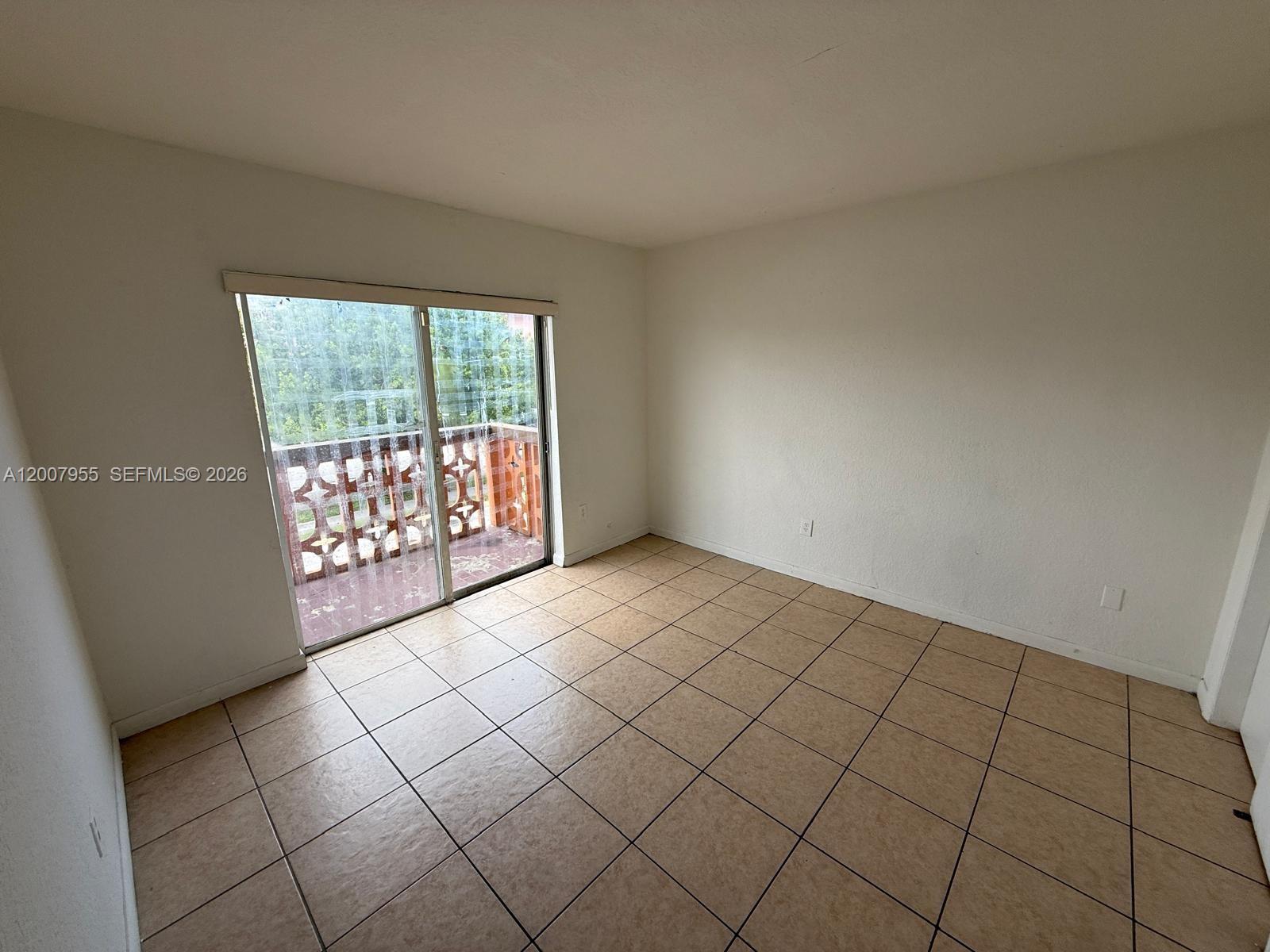 An empty room features beige tile flooring, white walls, and a sliding glass door to a balcony — 2330 NW 11th St # 33, Miami FL 33125, MIAMI, FL