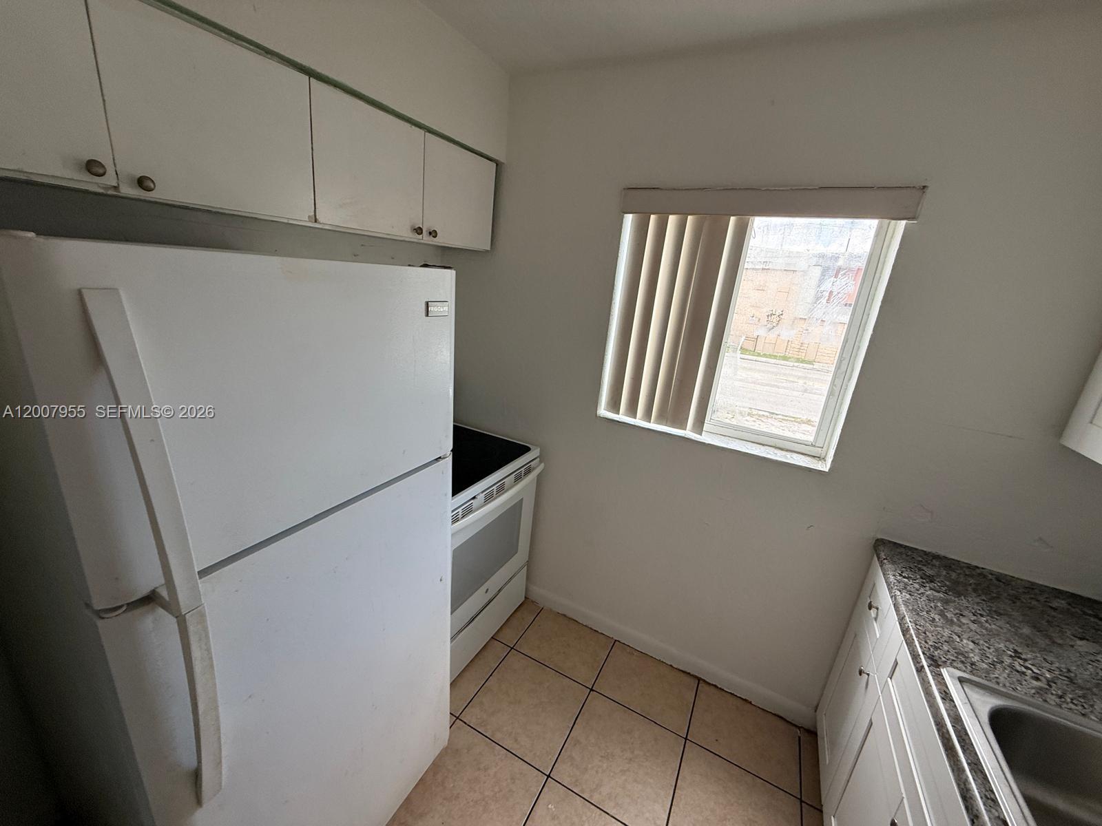 A small kitchen features a white refrigerator, stove, tiled floor, and granite-look countertops — 2330 NW 11th St # 33, Miami FL 33125, MIAMI, FL