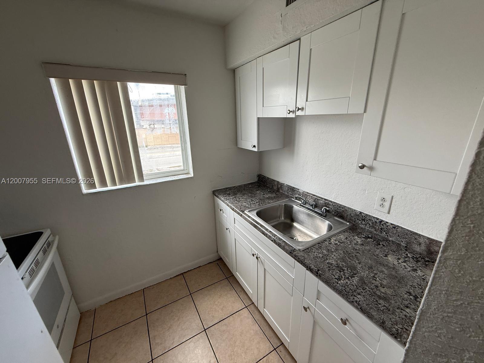 A small kitchen features white cabinets, a granite countertop, a stainless steel sink, and tile flooring — 2330 NW 11th St # 33, Miami FL 33125, MIAMI, FL