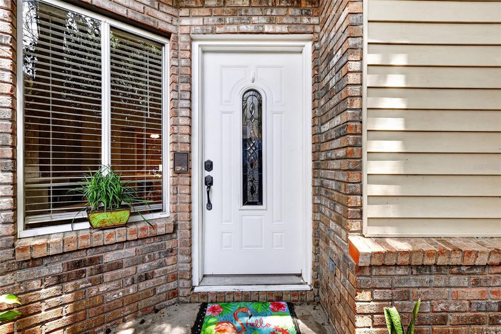 A white front door with a decorative glass insert sits between brick walls and siding — 2662 MCDONALD TERRACE, MOUNT DORA, FL