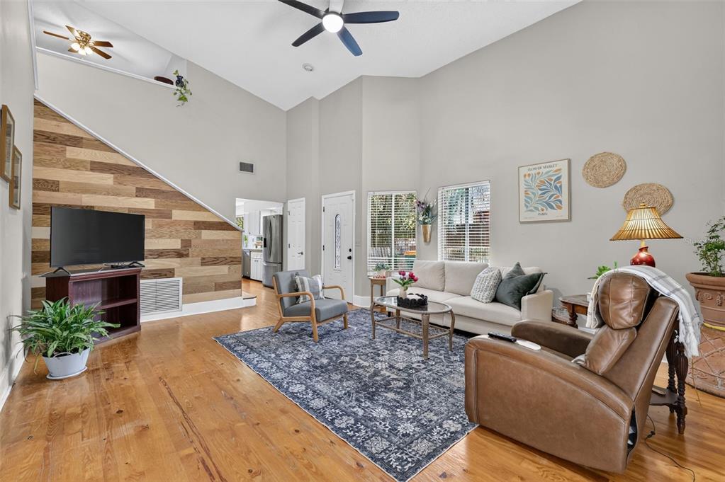 A living room with wood flooring, a wood-paneled accent wall, and a high vaulted ceiling — 2662 MCDONALD TERRACE, MOUNT DORA, FL