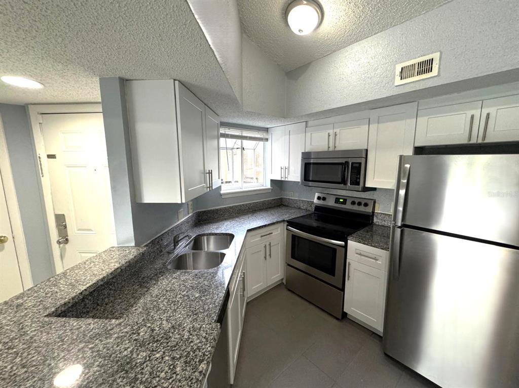 A kitchen features white cabinets, granite countertops, and stainless steel appliances — 1924 LAKE ATRIUMS CIRCLE UNIT 56, ORLANDO, FL