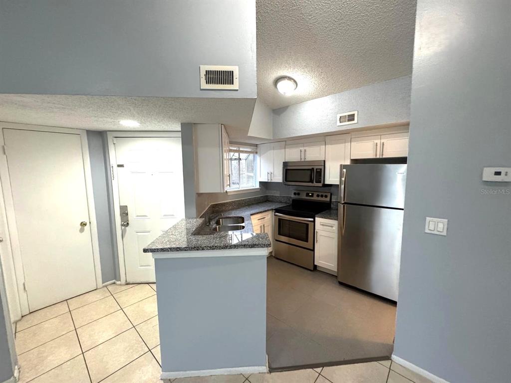 A kitchen with stainless steel appliances, granite countertops, and white cabinets — 1924 LAKE ATRIUMS CIRCLE UNIT 56, ORLANDO, FL