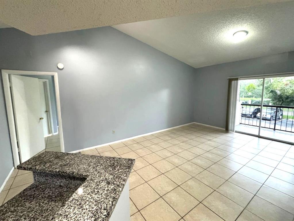 An empty living area features light blue walls, tile flooring, and a sliding glass door — 1924 LAKE ATRIUMS CIRCLE UNIT 56, ORLANDO, FL