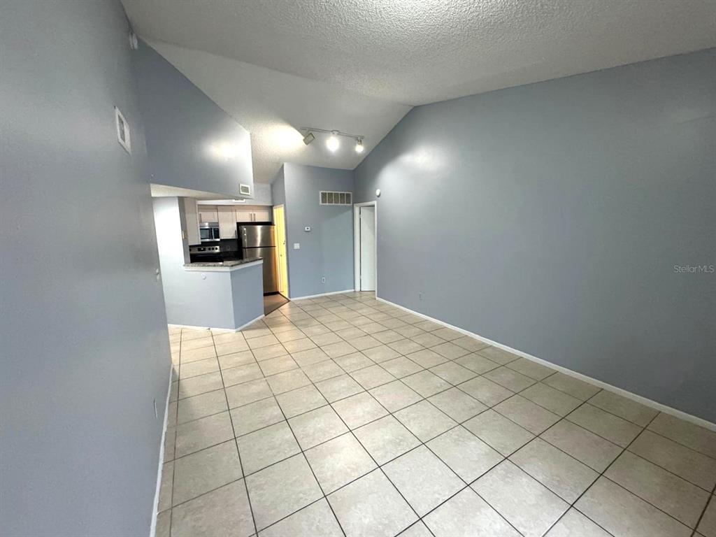 A room with light gray walls, tiled flooring, and an open kitchen in the background — 1924 LAKE ATRIUMS CIRCLE UNIT 56, ORLANDO, FL
