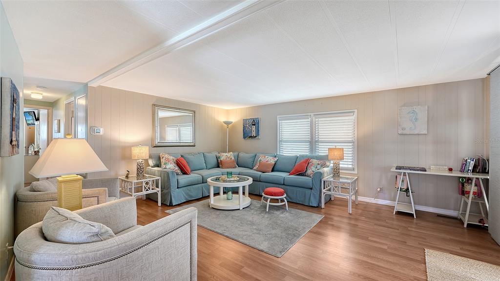 A living room features a blue sectional sofa, a gray area rug, and light wood flooring — 49 CABALLO WAY, BRADENTON, FL