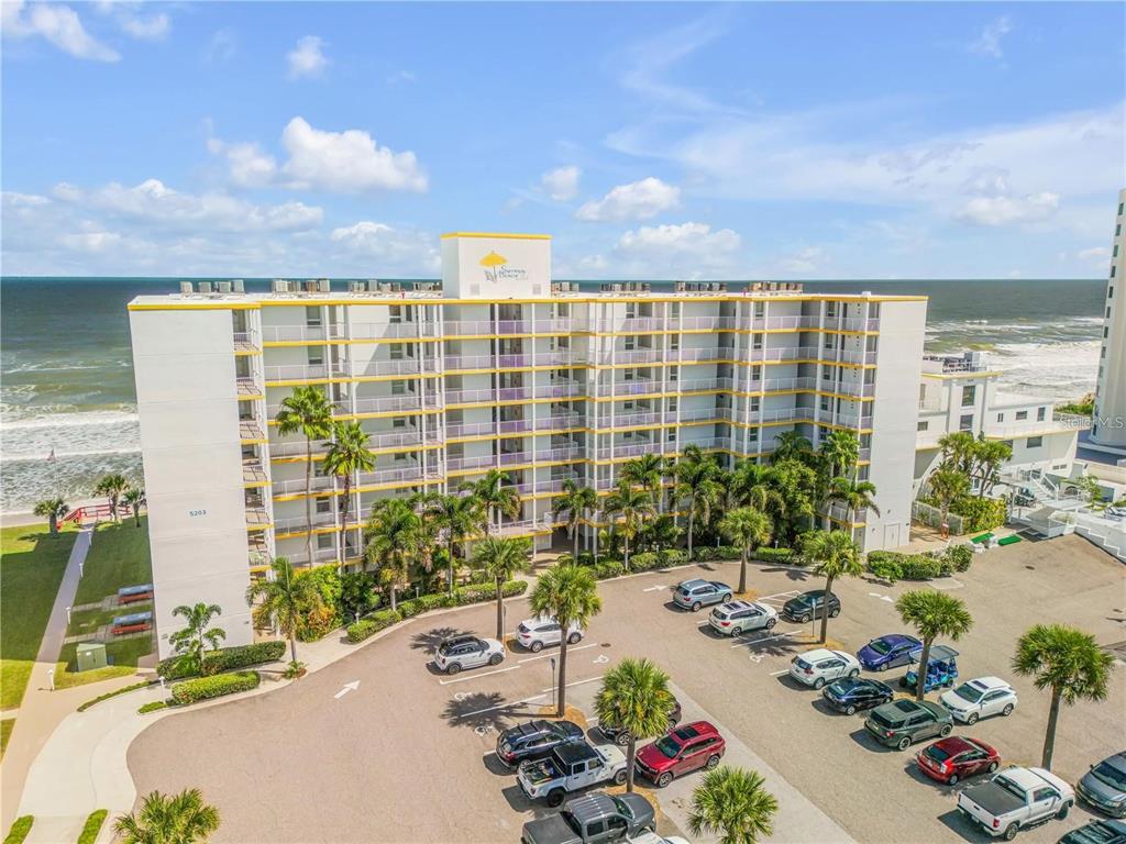 An aerial view of a multi-story beachfront condominium building with a parking lot in front — 5203 S ATLANTIC AVENUE UNIT 412B, NEW SMYRNA BEACH, FL