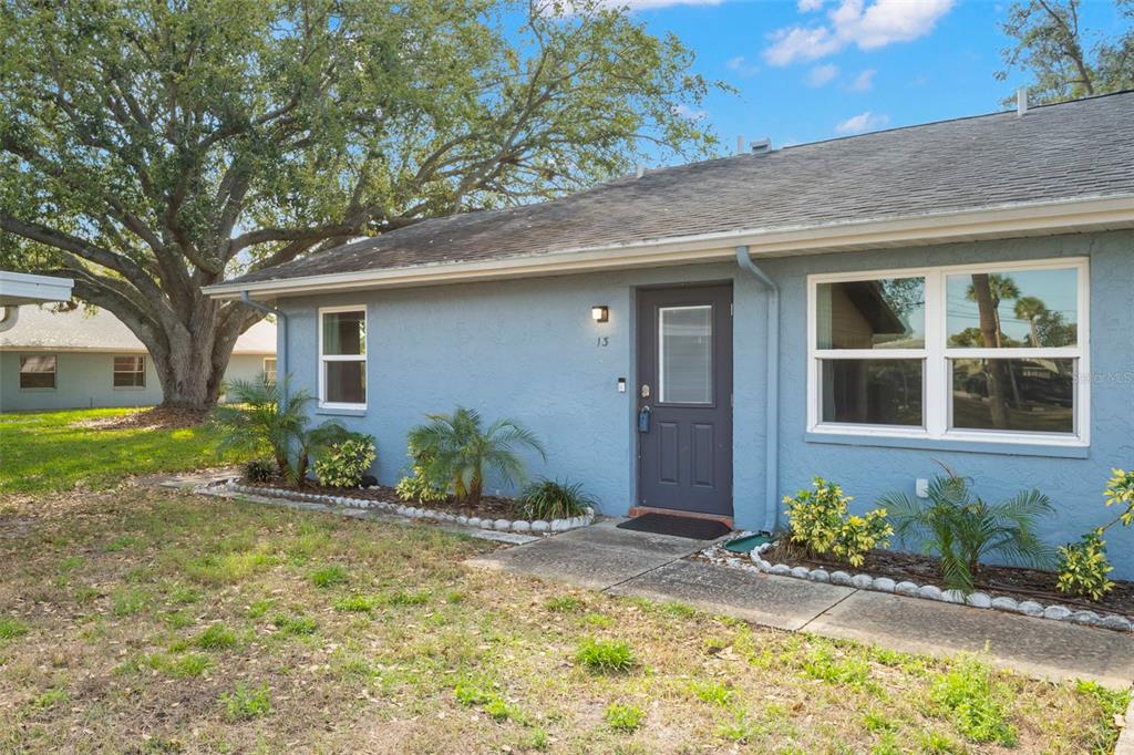 A light blue, single-story house exterior features a dark gray front door and white-trimmed windows — 1904 CANTERBURY LANE UNIT 13, SUN CITY CENTER, FL