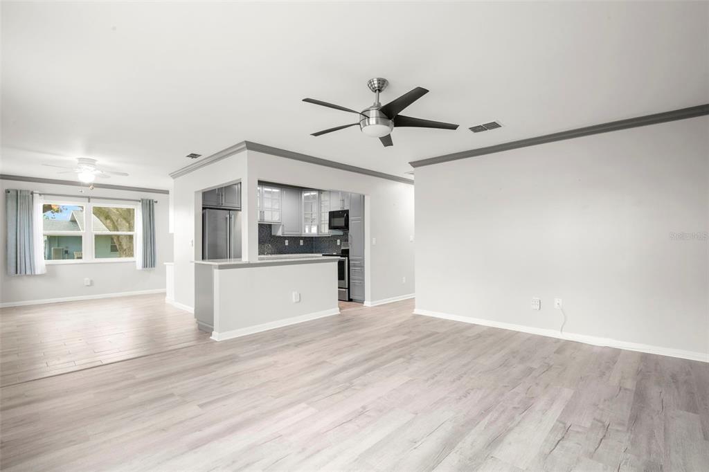 A living room with light wood-look flooring opens to a kitchen with gray cabinets — 1904 CANTERBURY LANE UNIT 13, SUN CITY CENTER, FL