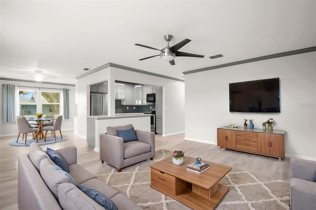 A living room with light wood floors, a grey sofa, and an open kitchen area — 1904 CANTERBURY LANE UNIT 13, SUN CITY CENTER, FL