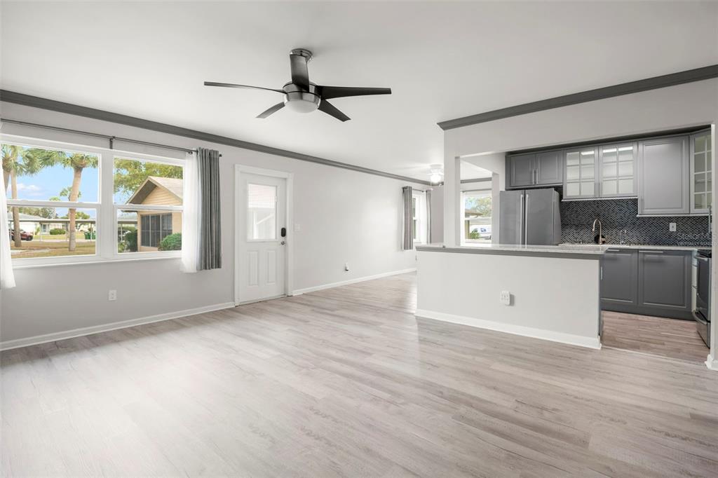 An open-concept living room with light wood flooring leads into a kitchen with gray cabinets — 1904 CANTERBURY LANE UNIT 13, SUN CITY CENTER, FL