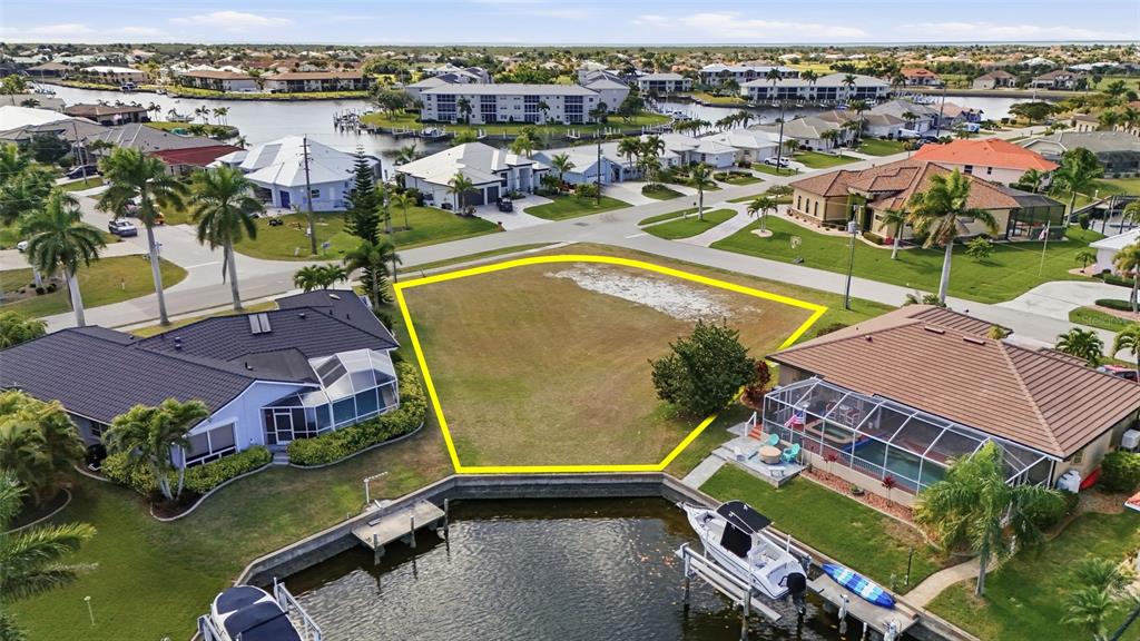 An aerial view shows a vacant waterfront lot outlined in yellow between two houses — 3460 OWL COURT, PUNTA GORDA, FL