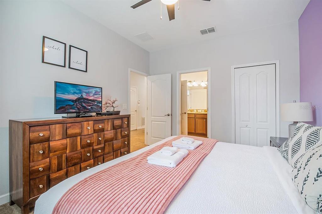A bedroom features a wooden dresser, a television, a bed with white linens, and an ensuite — 1433 THUNDERBIRD ROAD, DAVENPORT, FL