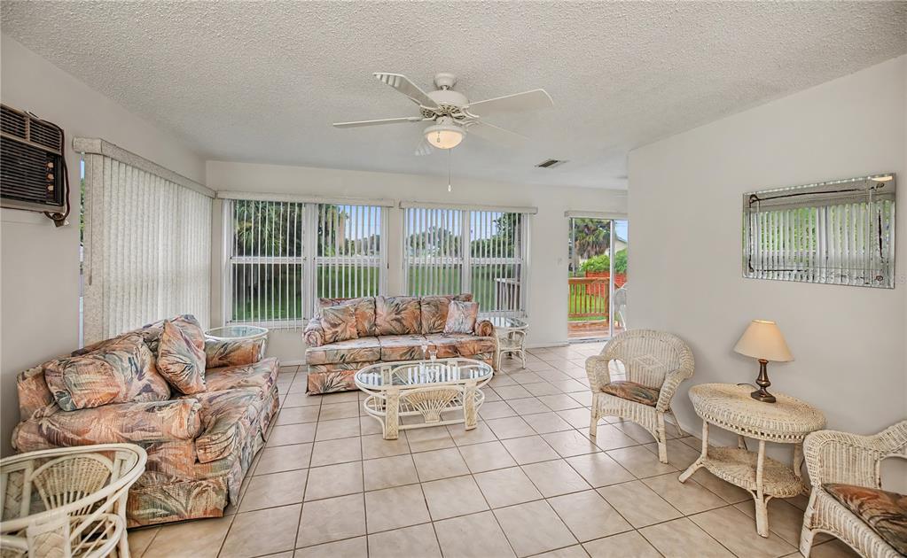 A sunroom features tile flooring, wicker furniture, floral sofas, and large windows overlooking a deck — 2828 MAGNOLIA WAY, PUNTA GORDA, FL