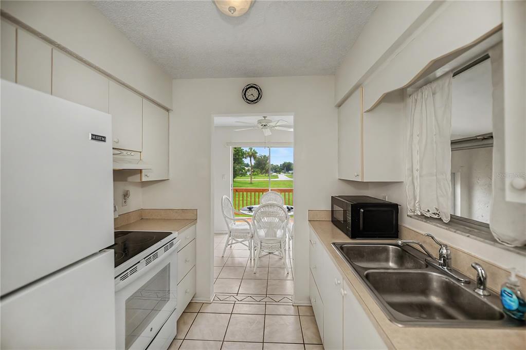 A galley kitchen with white cabinets and appliances leads to a dining area with patio access — 2828 MAGNOLIA WAY, PUNTA GORDA, FL