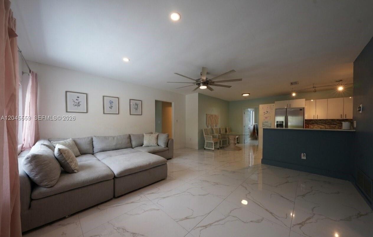 A spacious living room features light gray tile flooring, a large sectional sofa, and an open kitchen — 7304 Mckinley St, Hollywood FL 33024, HOLLYWOOD, FL