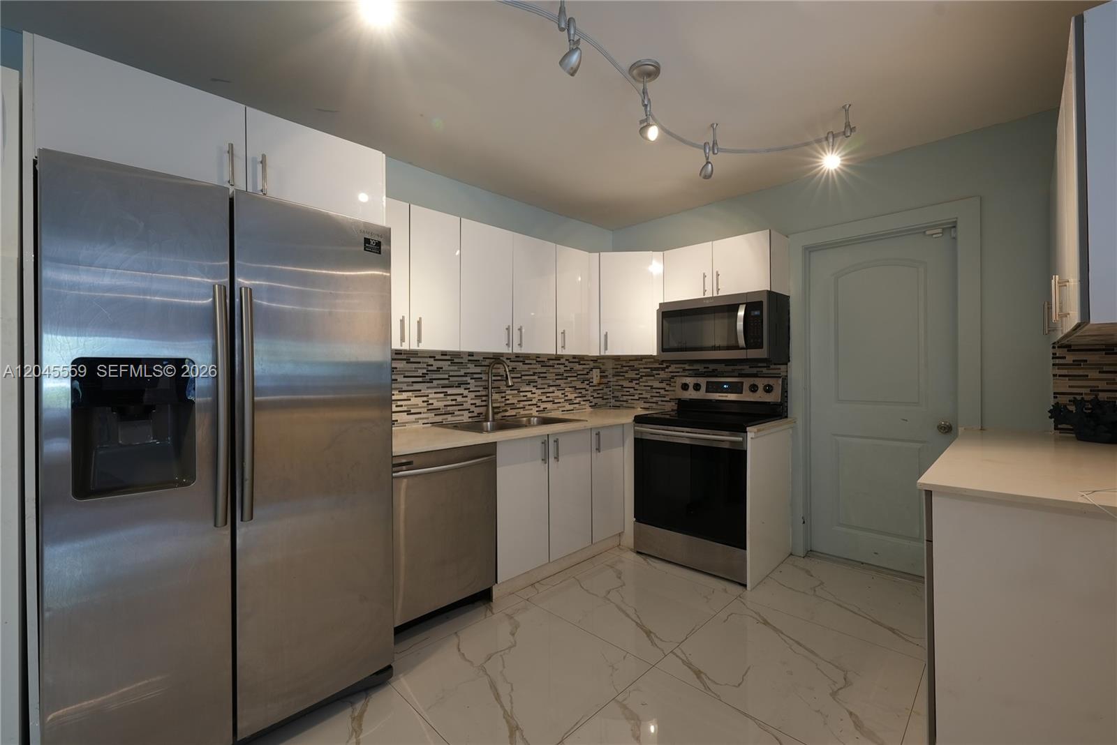 A kitchen features white cabinets, stainless steel appliances, a mosaic backsplash, and marble-look tile flooring — 7304 Mckinley St, Hollywood FL 33024, HOLLYWOOD, FL