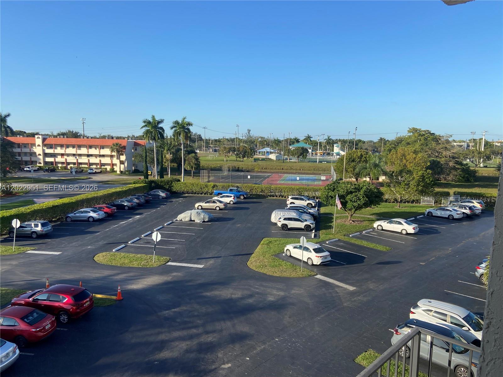 An elevated view of a parking lot featuring numerous cars, palm trees, and a tennis court — 7502 NW 30th Pl # 417, Sunrise FL 33313, SUNRISE, FL