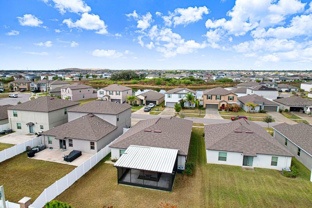 An aerial view shows suburban houses with fenced backyards and a pond in the distance — 13630 WILD GINGER STREET, RIVERVIEW, FL