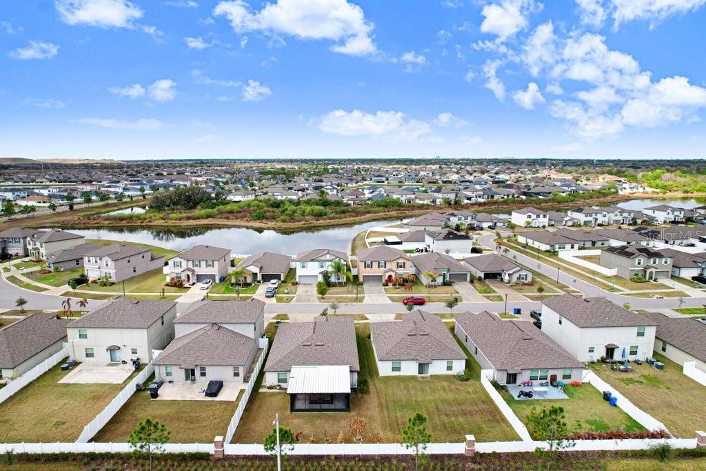 An aerial view shows a suburban neighborhood with houses, fenced backyards, and a central pond — 13630 WILD GINGER STREET, RIVERVIEW, FL
