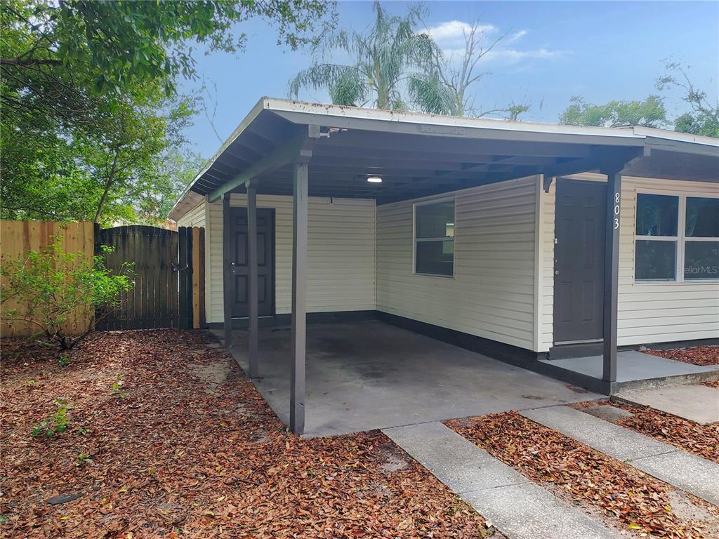 A carport with a concrete floor and a dark brown door attached to a house — 803 VALENCIA ROAD, PLANT CITY, FL