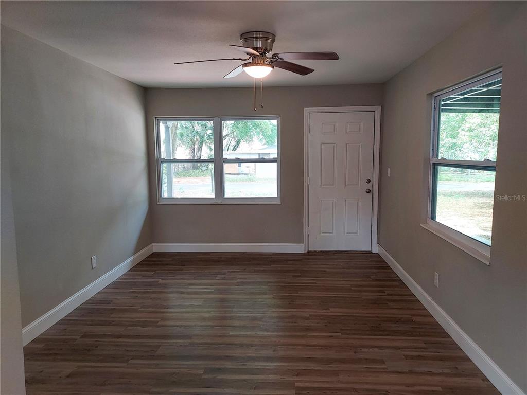 An empty room features wood-look flooring, a ceiling fan, a white door, and multiple windows — 803 VALENCIA ROAD, PLANT CITY, FL