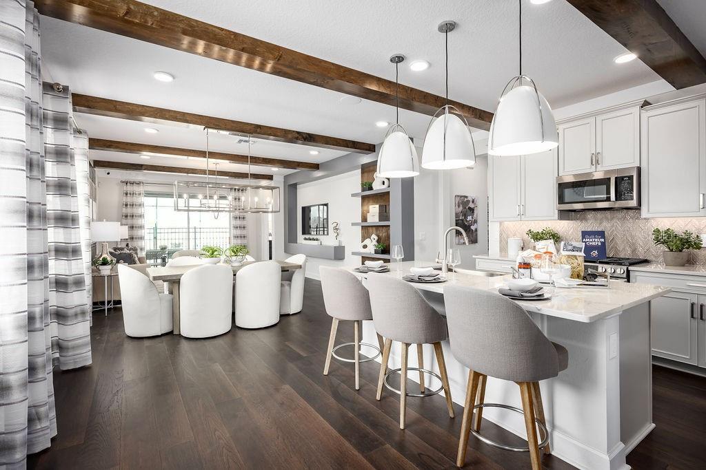 A kitchen with a white island and bar stools opens into a dining area with exposed beams — 5328 TEIRGARTEN STREET, ST CLOUD, FL