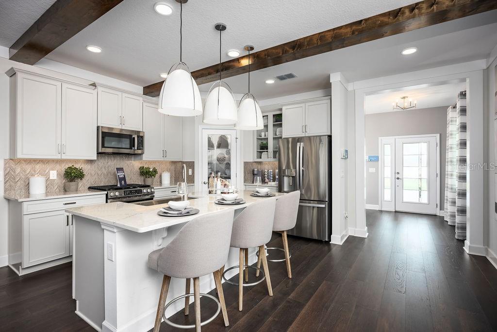 A modern kitchen features white cabinetry, a marble-topped island with bar stools, and wood beams — 5328 TEIRGARTEN STREET, ST CLOUD, FL
