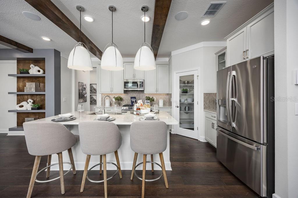 A modern kitchen features a central island with three stools, white cabinetry, and wood-beam ceilings — 5328 TEIRGARTEN STREET, ST CLOUD, FL