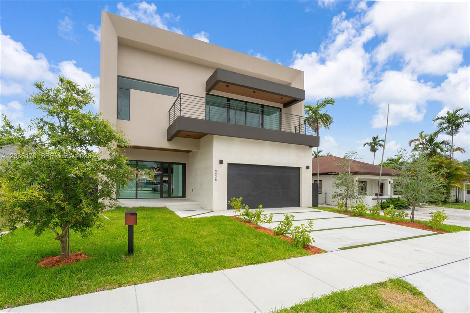 A modern two-story house features a dark garage door, a balcony, and a concrete driveway — 6438 SW 23rd St, Miami FL 33155, MIAMI, FL