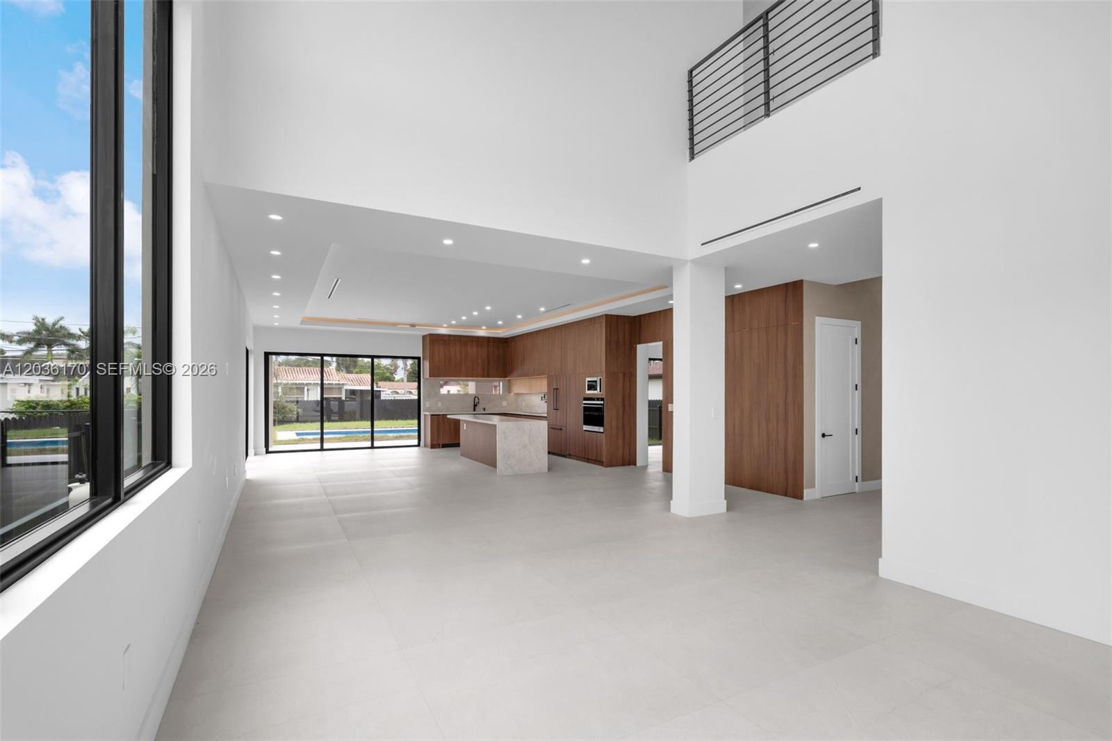 A modern open-concept kitchen features wood cabinetry, a stone island, and large sliding glass doors — 6438 SW 23rd St, Miami FL 33155, MIAMI, FL