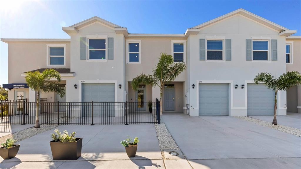 A row of two-story townhouses with light-colored stucco, gray garage doors, and small palm trees — 4060 GOLD DUST LANE, SARASOTA, FL