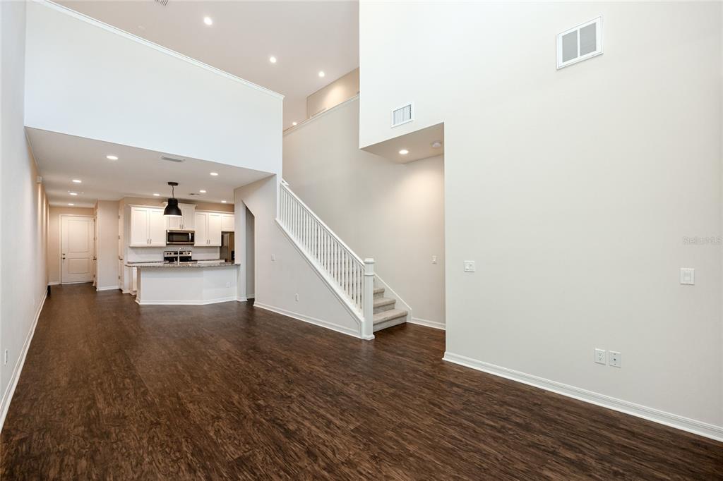 A living area with dark wood floors, a staircase, and an open kitchen in the background — 1510 FIGLEAF LANE, CLEARWATER, FL