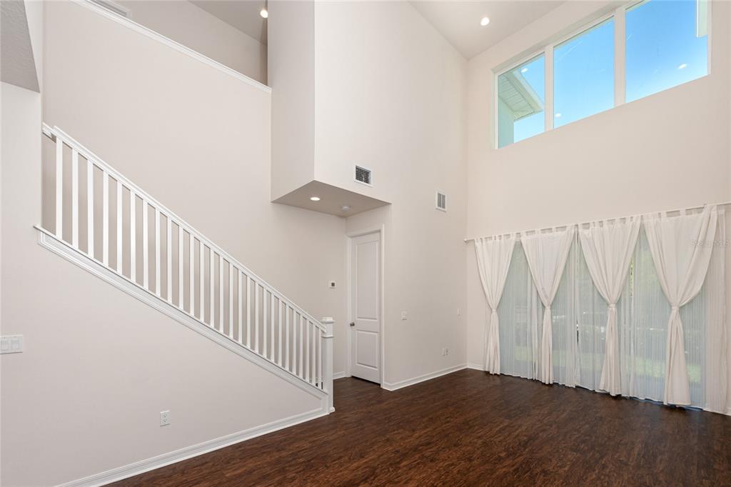 A bright living room features high ceilings, dark wood flooring, a staircase, and large windows — 1510 FIGLEAF LANE, CLEARWATER, FL