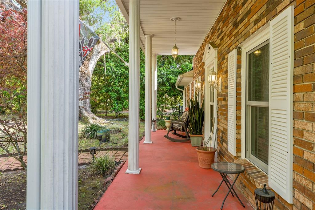 A covered brick porch features white columns, a red floor, and a rocking chair — 1008 S MILDRED AVENUE, BROOKSVILLE, FL