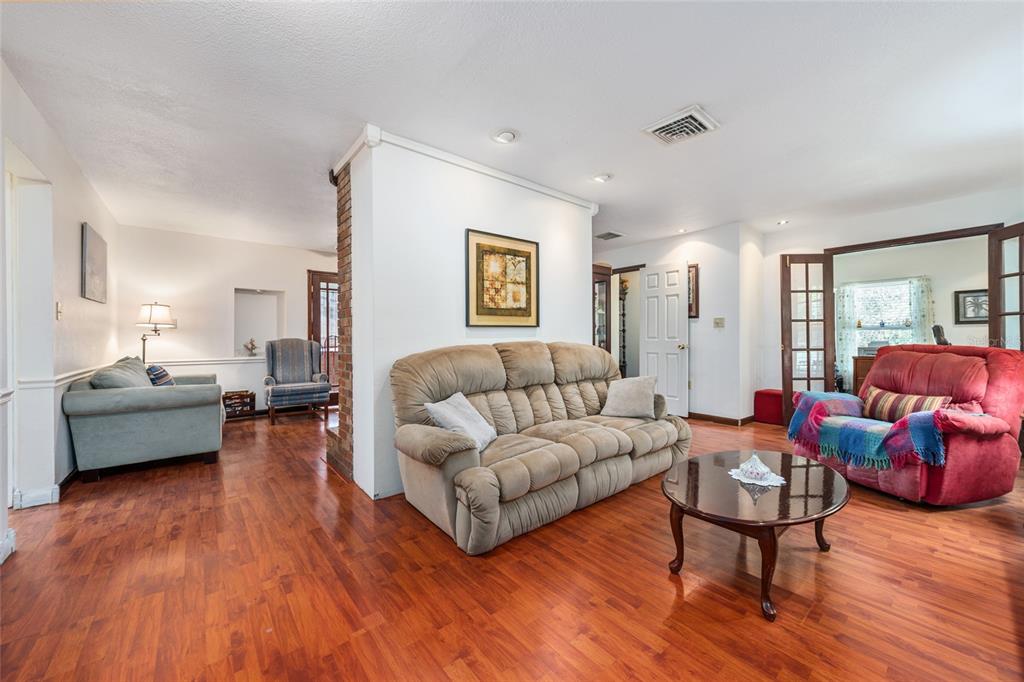 A living room features hardwood floors, a beige sofa, a red recliner, and a brick pillar — 1008 S MILDRED AVENUE, BROOKSVILLE, FL