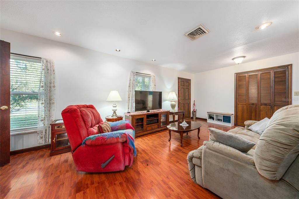 A living room features wood flooring, a red recliner, a beige sofa, and wooden cabinets — 1008 S MILDRED AVENUE, BROOKSVILLE, FL