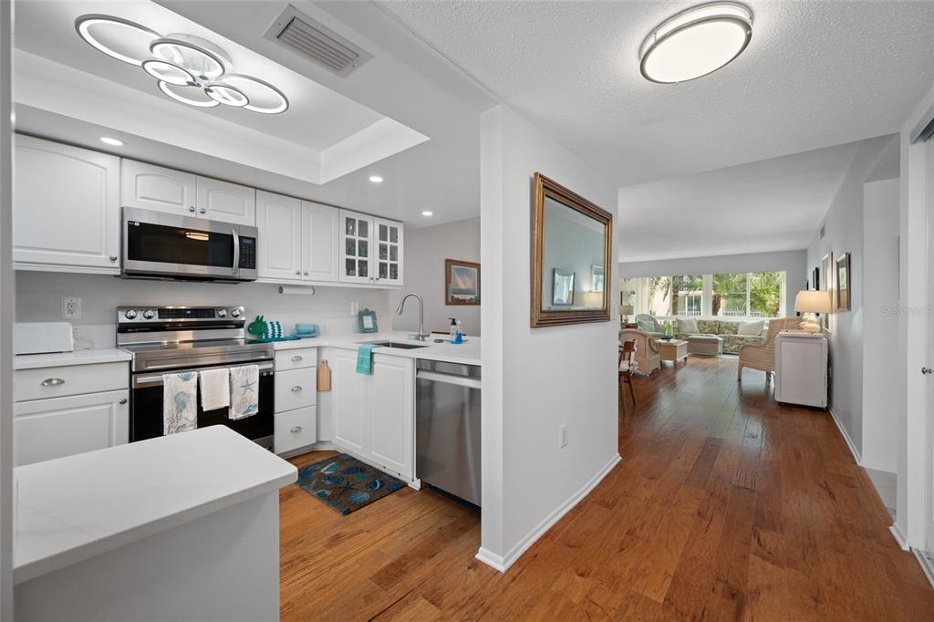 A white kitchen with stainless steel appliances opens into a living area with hardwood floors — 121 ISLAND WAY UNIT 323, CLEARWATER BEACH, FL