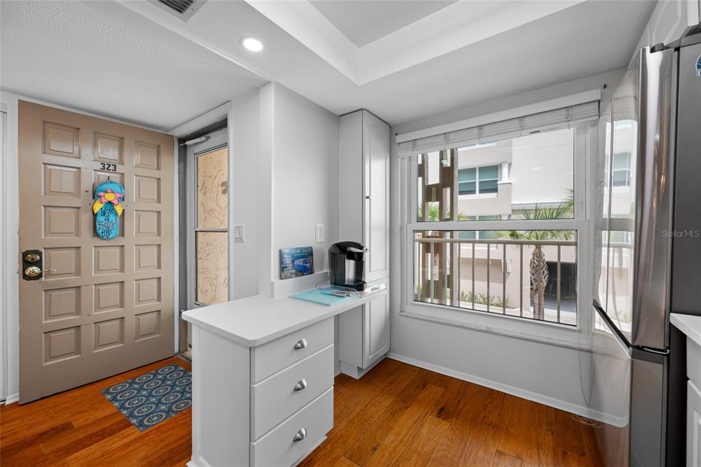 A kitchen area features white cabinets, a coffee maker, wood flooring, and a glass door — 121 ISLAND WAY UNIT 323, CLEARWATER BEACH, FL