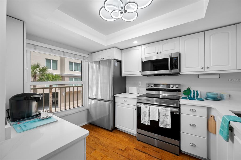 A kitchen features white cabinets, stainless steel appliances, wood flooring, and a window with exterior views — 121 ISLAND WAY UNIT 323, CLEARWATER BEACH, FL