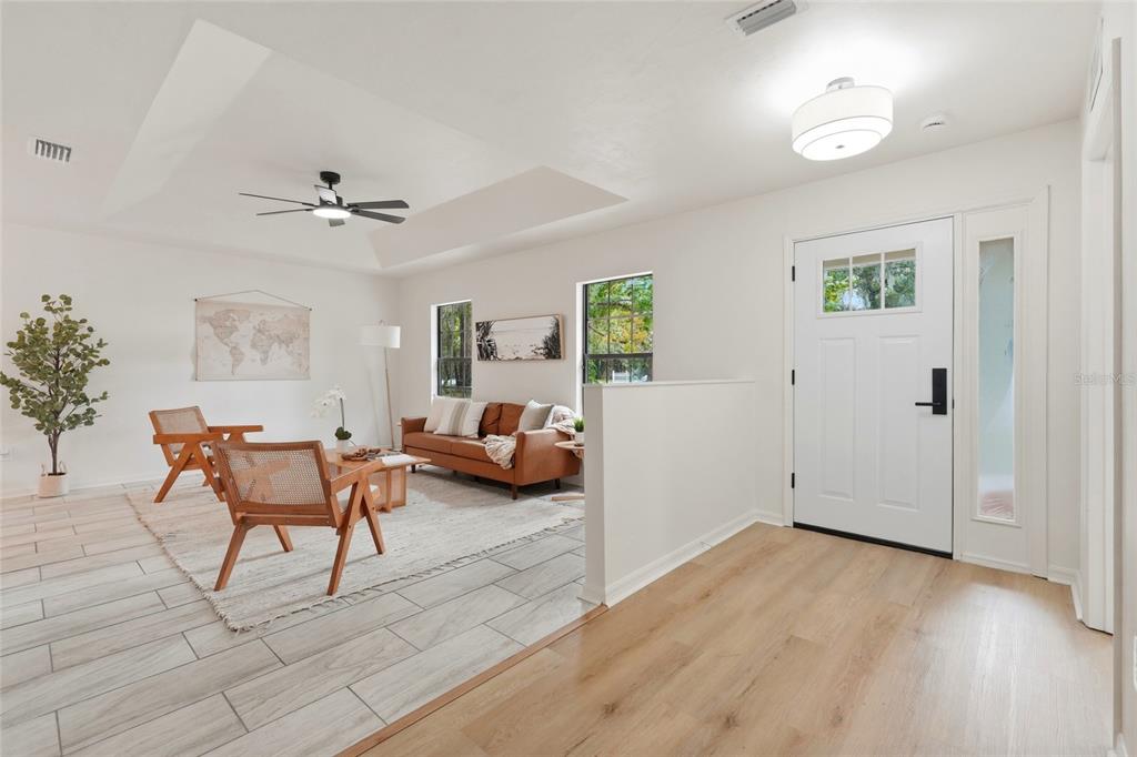 A bright entryway leads into a living room with wood-look tile flooring and a tray ceiling — 5813 SE 230TH TERRACE, HAWTHORNE, FL