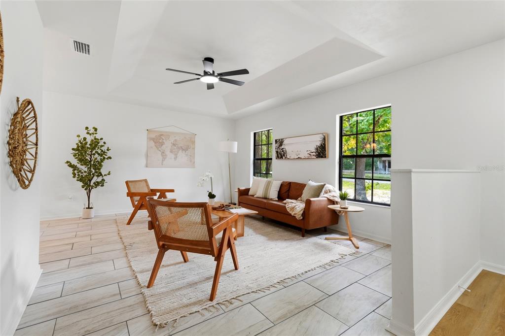 A bright living room features a brown leather sofa, two wooden chairs, and a ceiling fan — 5813 SE 230TH TERRACE, HAWTHORNE, FL