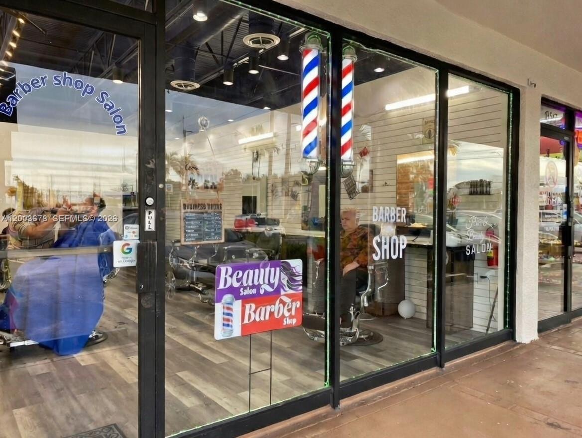 The exterior view of a storefront featuring glass doors, barber poles, and signage for a salon — AVENTURA, FL