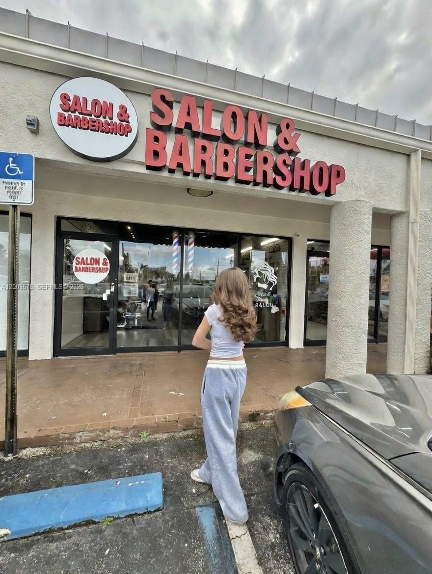 A person stands in front of a commercial storefront labeled Salon & Barbershop — AVENTURA, FL