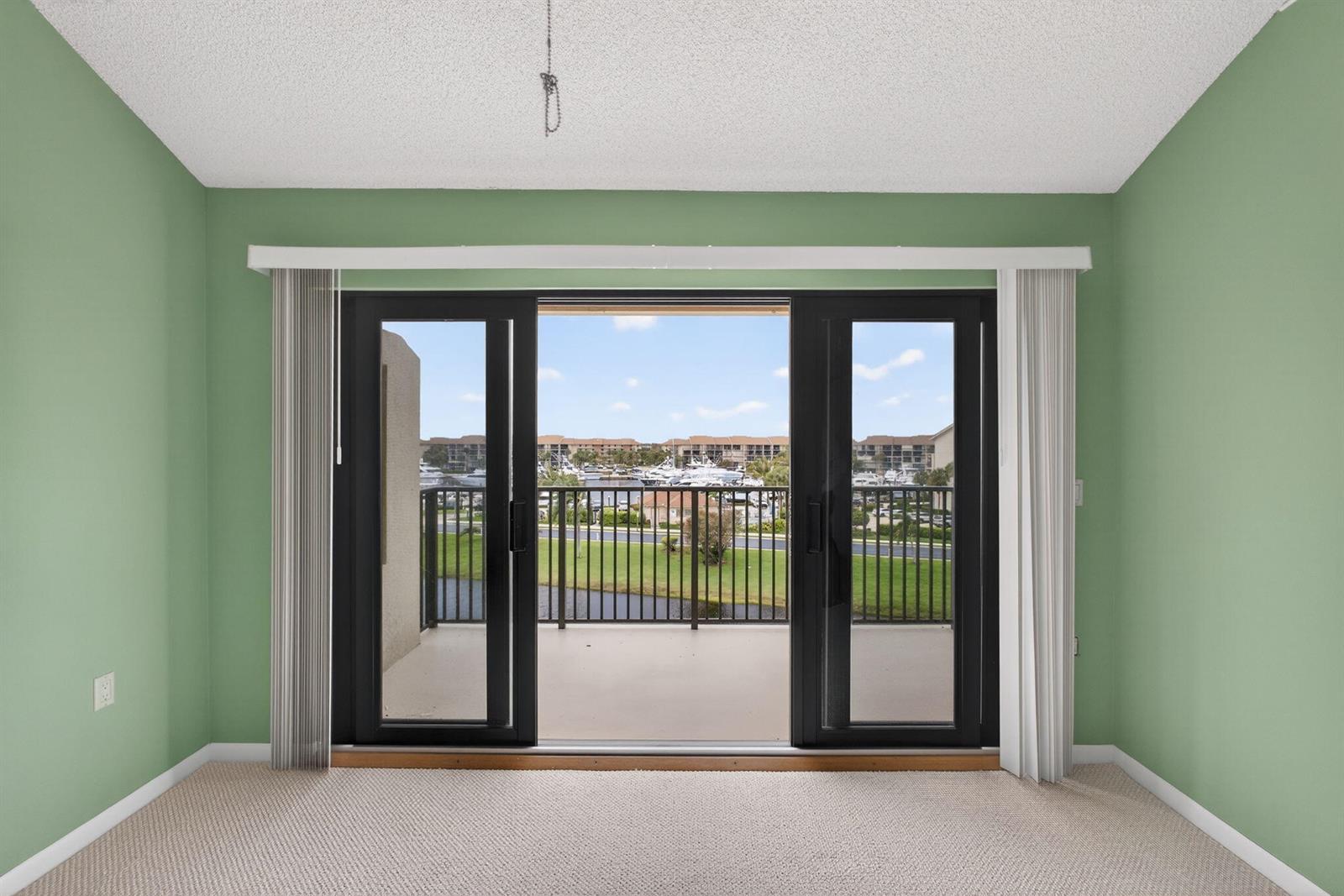An empty room with green walls and carpet features a sliding glass door to a balcony — 601 Seafarer Circle # 504, Jupiter FL 33477, JUPITER, FL